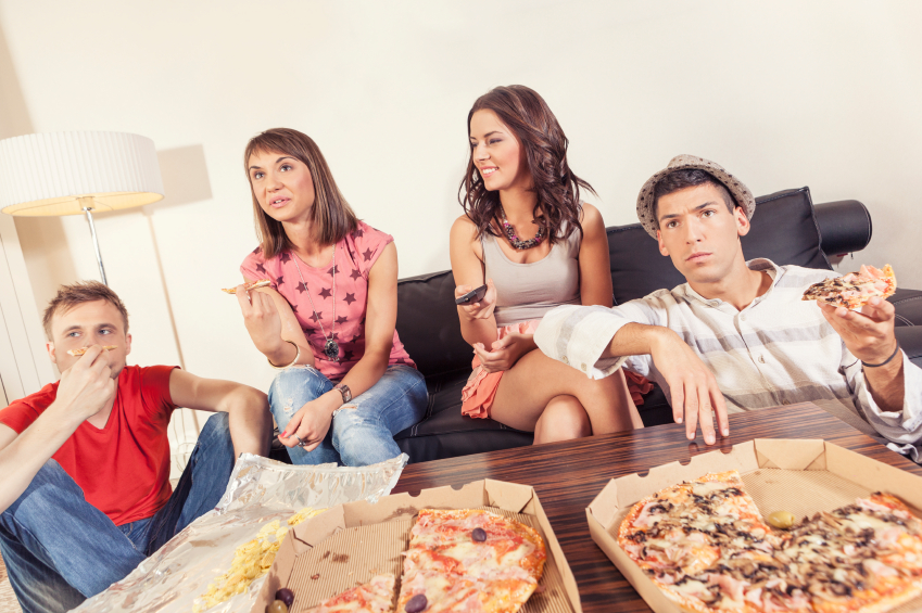 Friends eating pizza and watching TV at home
